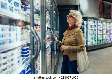 Mature Woman Shopping In Grocery Store. Woman Choosing Food From Fridge In Supermarket.