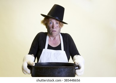 Mature woman with singed face holding roasting pan with pilgrim hat and apron.