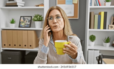 A mature woman sips coffee while talking on the phone in her modern office, indicating busy professional life. - Powered by Shutterstock