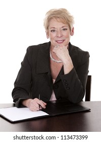 Mature Woman Sitting Behind Desk And Writing Notes Down