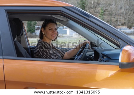 A mature woman sitting behind the wheel of a car smiling and looking at camera