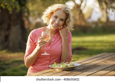 A Mature Woman Sitting At A Garden Bench Eating A Meal