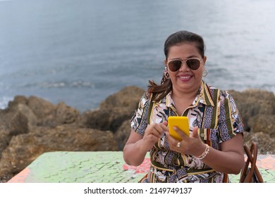 Mature Woman Sitting On Bench Checking Cell Phone In Park