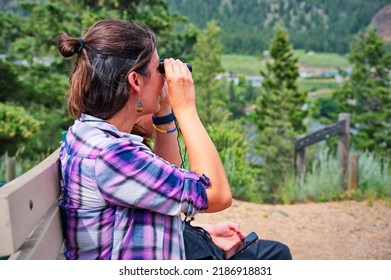 Mature Woman Sitting On The Bench And Using Binoculars