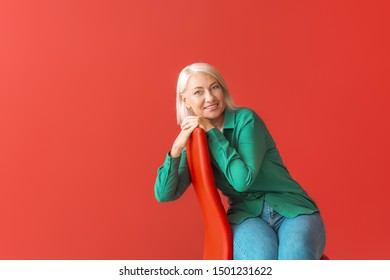 Mature Woman Sitting On Chair Against Color Background