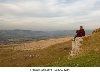 Mature woman sitting on cliff top overlooking rural view - Shutterstock ID 1331076284