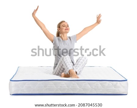 Mature woman sitting on soft mattress against white background