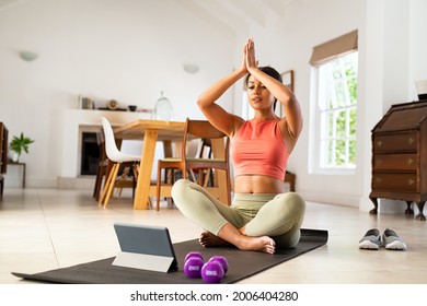 Mature Woman Sitting On Yoga Mat And Looking At Digital Tablet For Online Lessons Of Hata Yoga. Healthy Mid Adult Black Woman Practicing Yoga With Online Trainer At Home. African Lady Practicing Yoga.