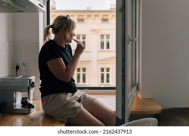 Mature Woman Smoking E Cigarette At Home Near The Window. Caucasian 40 50 Years Old Female Smoker