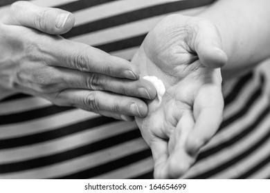 Mature Woman Spread Out Skincare Cream To Her Hand, Horizon Format Black And White Image