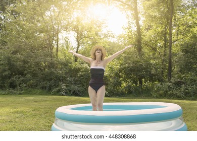 Mature Woman Standing In Paddling Pool, Arms Outstretched