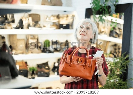 Mature woman in store eye windowshopping product she likes and tactilely checks authenticity and naturalness of leather material from which bag is made. Buyer examines quality of material
