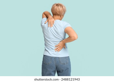 Mature woman suffering from back pain on blue background. Back view - Powered by Shutterstock