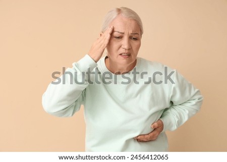 Mature woman suffering from breast pain on beige background. Cancer awareness concept