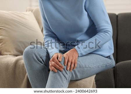 Mature woman suffering from knee pain on sofa indoors, closeup. Rheumatism symptom