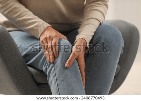 Mature woman suffering from knee pain in armchair, closeup. Rheumatism symptom