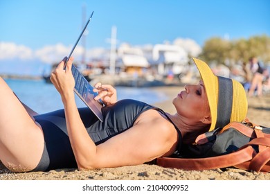 Mature Woman Sunbathing On The Beach In Hat With Laptop