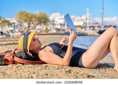 Mature Woman Sunbathing On The Beach In Hat With Laptop