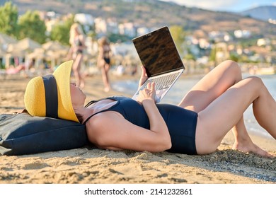 Mature Woman Sunbathing On The Beach Using A Laptop