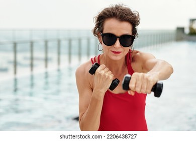 Mature Woman In Swimsuit Working Out With Dumbbels By Swimming Pool