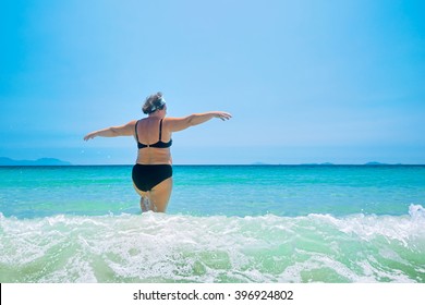 mature woman in swimwear at the sea. Overweight woman in swimsuit comes in water in time of surf, rear view
