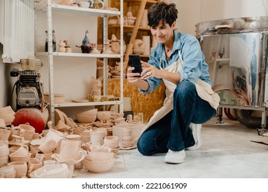 Mature Woman Taking Picture Of Handcrafts While Sitting At Pottery Workshop