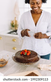 Mature Woman Taking Pictures Of A Cake In The Kitchen. Female Capturing Photos Of Chocolate Cake With Her Mobile Phone.