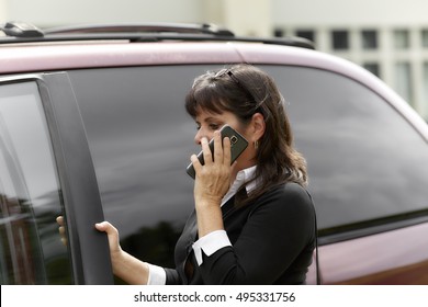 Mature woman talking on cell phone holding the car door open to enter - Powered by Shutterstock