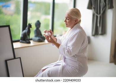 Mature Woman In The Terry Bathrobe Applying A Skincare Product