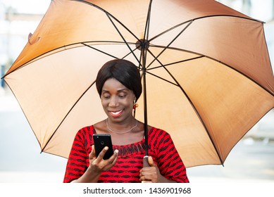 mature woman in traditional clothes standing looking at mobile phone smiling with umbrella over her head. - Powered by Shutterstock