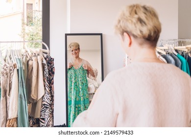 Mature Woman Trying On Clothes In Front Of A Mirror. Blonde Woman Shopping In A Fashion Shop. Shopping Concept.