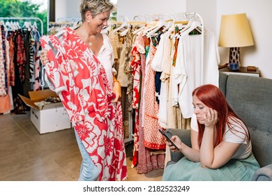 Mature Woman Trying On Clothes Happy, Young Woman Bored Waiting For Her Friend To Finish Shopping For Clothes. Mother And Daughter Shopping In A Clothing Shop. Concept Of Shopping.
