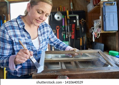 Mature Woman Upcycling Furniture In Workshop At Home  Painting Cabinet         