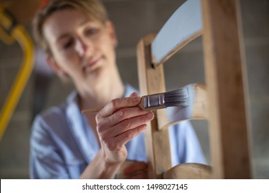 Mature Woman Upcycling Furniture In Workshop At Home  Painting Wooden Chair             