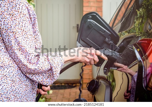 Mature woman using electric charging point at home to\
fuel electric car
