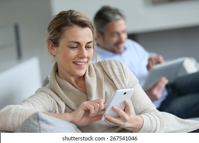 Mature woman using smartphone, husband in background