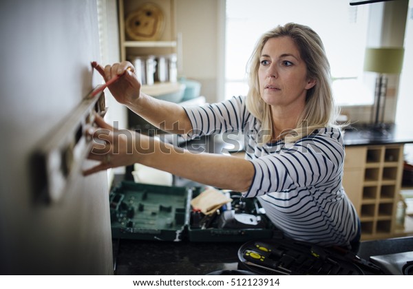 Mature woman using a spirit level and\
marking the wall with a pencil in her\
kitchen.