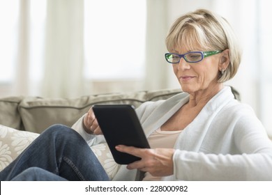 Mature Woman Using Tablet Computer While Relaxing On Sofa At Home