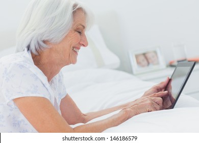 Mature woman using a tablet while she is lying on bed - Powered by Shutterstock