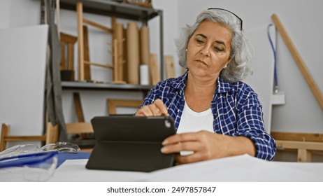 Mature woman using tablet in a woodworking workshop, showcasing creativity and technology integration. - Powered by Shutterstock