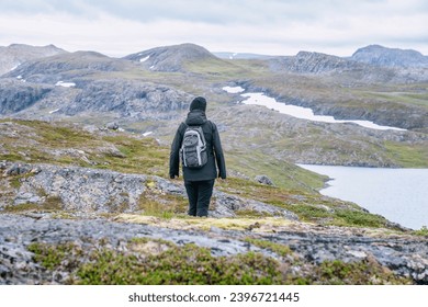 Mature woman walks down over high altitude Norwegian Mountains range terrain. Hiking high in Norwegian mountains. Healthy lifestyle. Norway, Krutvatnet. Rear view