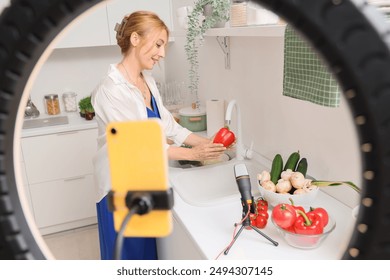 Mature woman washing bell pepper while recording cooking video class in kitchen - Powered by Shutterstock