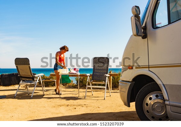 Mature
woman washing up dishes in bowl on fresh air at camper car.
Dishwashing outdoor on camping site, sea
shore