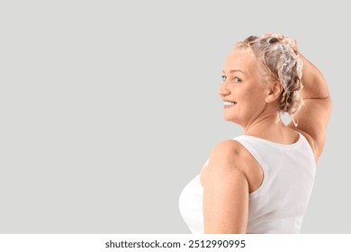 Mature woman washing hair on light background - Powered by Shutterstock