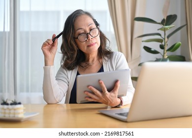 Mature Woman Wearing Eyeglasses Watching Online Webinar, Managing Domestic Bills And Home Finance On Digital Tablet