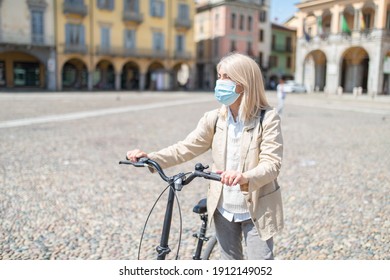 Mature Woman Wearing Face Medical Mask While Riding A Bicycle During Covid Pandemic Outdoors