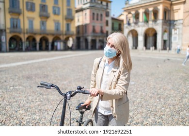 Mature Woman Wearing Face Medical Mask While Riding A Bicycle During Covid Pandemic Outdoors