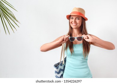 Mature Woman Wearing Hat Standing Studio Isolated On White Wall Carrying Beach Bag Holding Sunglasses Looking Camera Smiling Happy