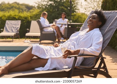 Mature Woman Wearing Robe Outdoors On Lounger Drinking Champagne On Spa Day