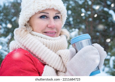 Mature Woman Wearing White Hat Drinks Hot Drink From Travel Mug Enjoying Frosty Weather Closeup. Snowy Winter Forest At Heavy Snowfall, Close-up